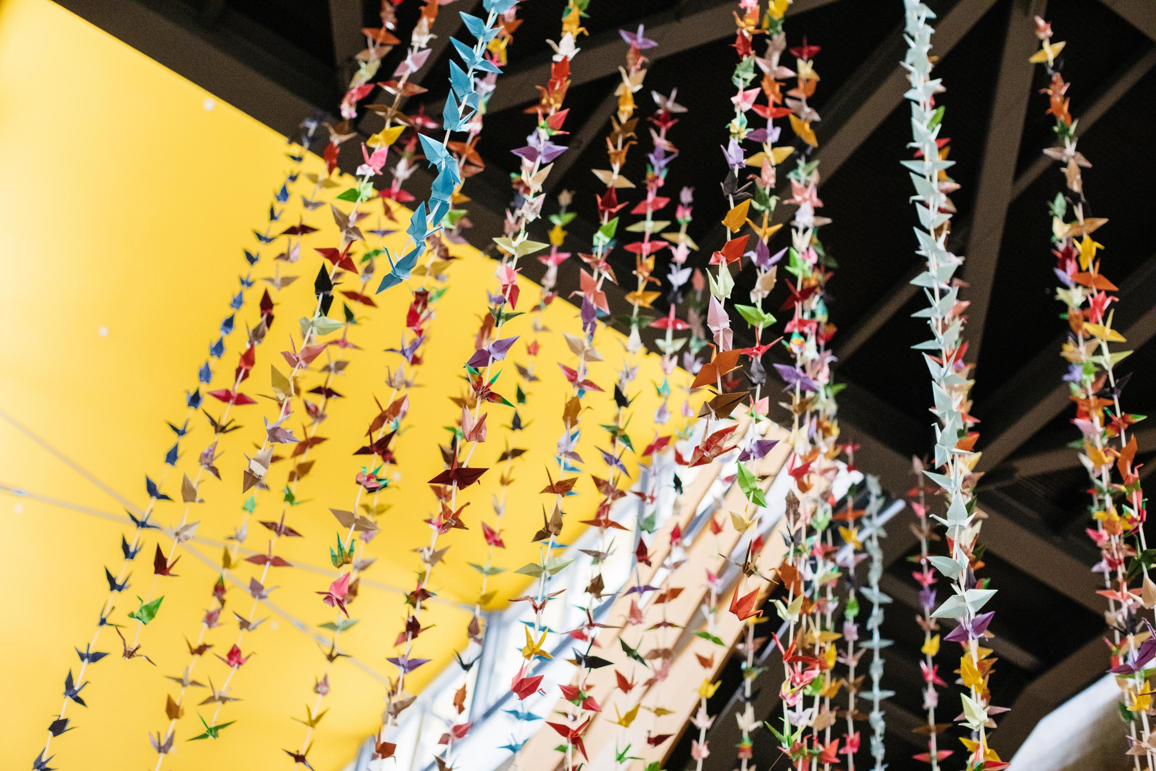 view facing upward of art installation of origami cranes of various colors hung from ceiling